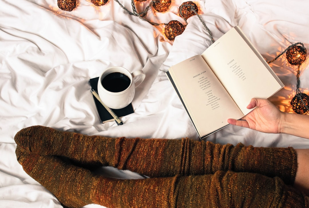 Person wearing stockings in bed reading a book with coffee